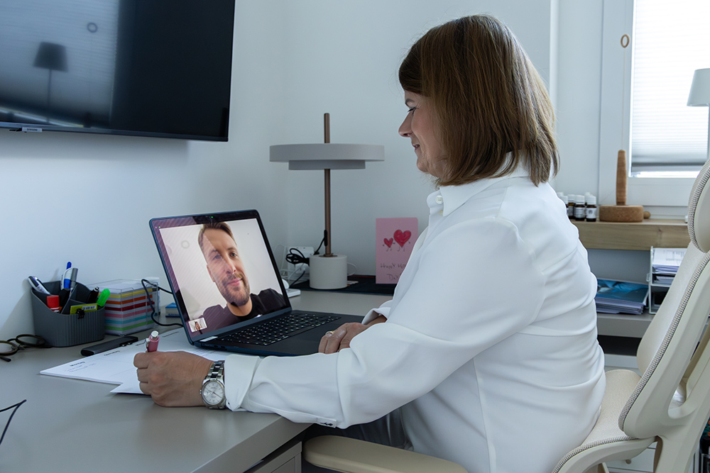 Katja Böcker sitzt an ihrem Schreibtisch und führt ein Videogespräch mit einem Klienten auf dem Laptop